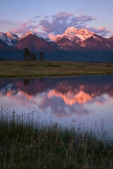 Snow-capped peaks of the Mission Mountain Range reflected in a small pond near Ronan, Lake County, Montana, USA