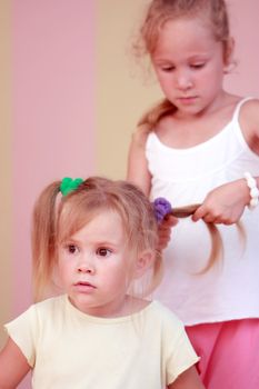 Small girl getting hair comb by sister at home