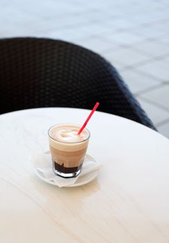 Glass of cappuccino standing on ring table near chair