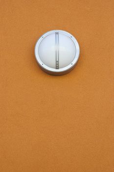 Round modern light fixture on orange stucco wall