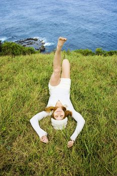 Joyful young woman relaxing in grass near ocean in Maui, Hawaii.