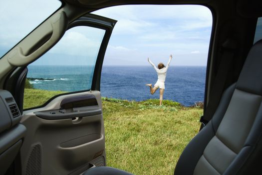 Excited woman standing on grassy cliff by Pacific Ocean in Maui, Hawaii.