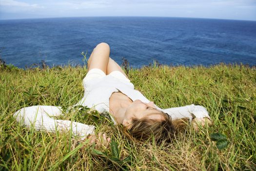 Portrait of young redheaded woman relaxing in grass above the ocean in Maui, Hawaii.