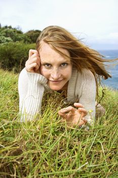 Portrait of young redheaded woman lying in grass looking at viewer with devilish grin.