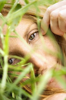 Close up portrait of pretty redhead lying in grass looking at viewer.