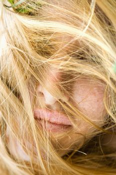 Close up portrait of redheaded woman with windblown hair covering face.