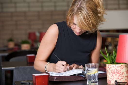 Pretty blond woman writing in her notebook sitting in a restaurant