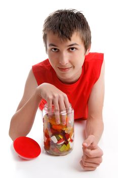 A boy places his hand into a lolly jar filled with a variety assortment of soft sweet confectionery.  