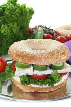 Bagel with Camembert cheese, tomato, cucumber, cream cheese and lettuce on white background