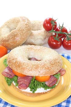 Bagel with salami, peppers, cream cheese and lettuce on white background