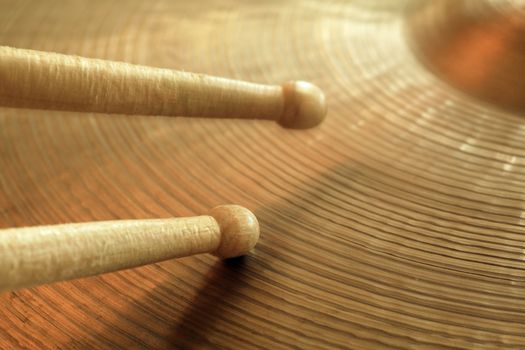 Photo of two drumsticks playing on a hi-hat or ride cymbal.  Focus on tip of lower stick while other stick has slight motion.