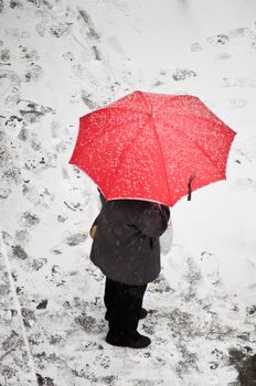 Woman with red umbrella standing on a snow covered sidewalk