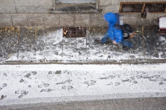 Passer by walking on a snowy day in a street. View from above.