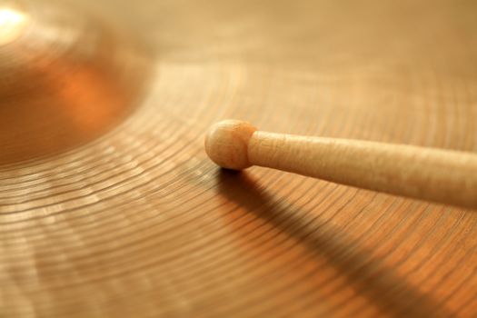 Photo of a drumstick playing on a hi-hat or ride cymbal.  Focus on tip of stick.