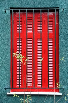 Red wooden window shutter and protective metal bars.