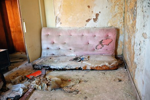 Broken couch and peeling paint wall. Abandoned house interior.