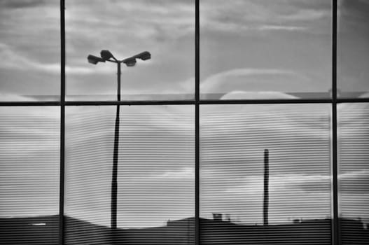 Overcast sky and street lights mirrored on the glass windows of a modern office building. Architectural detail.