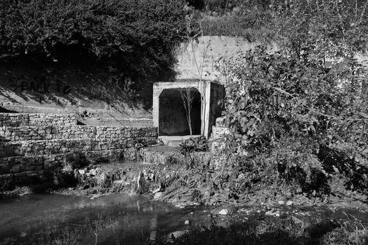 Waste water and sludge from a drain contaminating a small river. Black and white.