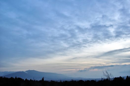 Distant city lights and foggy mountain horizon under sunset colored sky.
