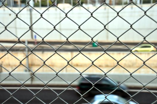 Speeding cars on the motorway seen through wire mesh fence. Motion blur.