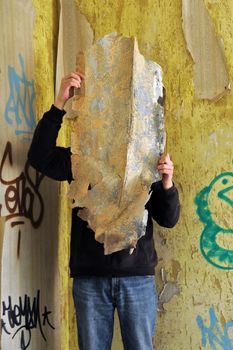 Obscured male figure in abandoned house. Vintage wallpaper shreds.