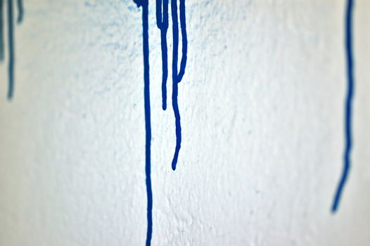 White wall with blue dripping paint. Selective focus.