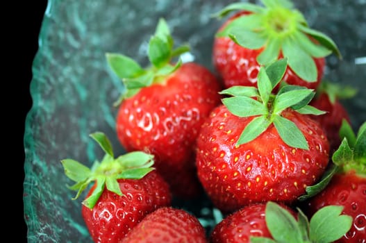 Glass bowl with fresh strawberries on black background. Selective focus macro.