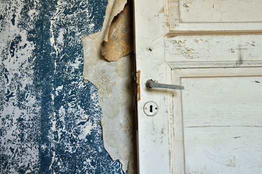 Torn vintage wallpaper peeling paint wall and wooden door in abandoned house.
