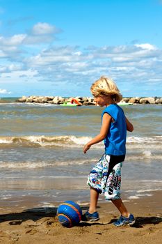 a boy is playing football on the beach on a sunny day