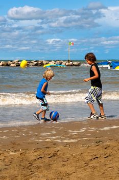 two boys playing football on the beach on a sunny day