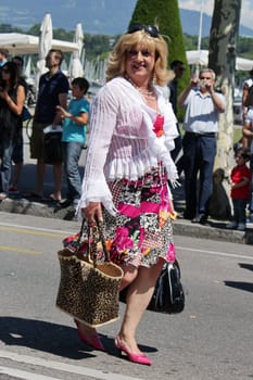 Man dressed up as a woman with a blond wig, a colorful skirt, two big bags, pink heel shoes and walking in the street at the Gay Pride parade 2011, Geneva, Switzerland