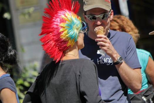 One eprson wearing a colorful punk wig and talking to another eating an icecream at the Gay Pride 2011, Geneva, Switzerland