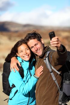 Happy young couple smiling hiking outdoors on travel taking selfportrait picture with compact camera or mobile phone. Mixed race Asian Caucasian couple on holidays. Photo from volcano Teide, Tenerife, Canary Islands.