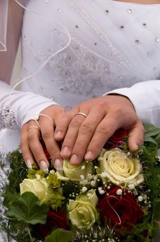 Hands of newlyweds with a bouquet of flowers.