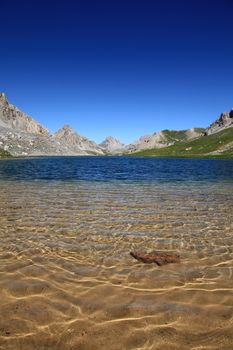 Translucent lake of mountain with some sand and a rock in foreground.