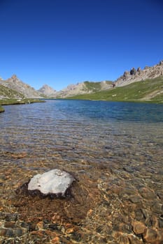 A translucent lake in mountains with a rock in foreground.