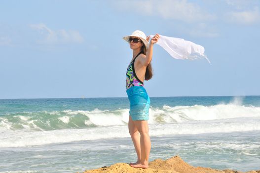 A girl stands on the beach and holding a white scarf that develops in the wind