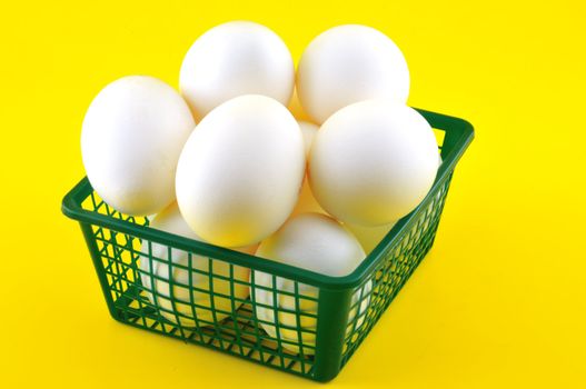 White eggs are in a plastic basket against a yellow background