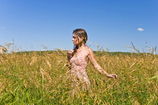 Beautiful young woman in a field of rye. Touch the ears harvest by hand. Rural landscape.