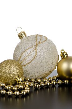 Golden christmas balls with decorations on black surface and white backdrop.