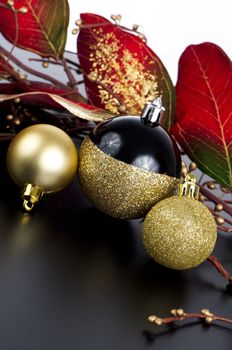 Golden christmas balls with decorations on black surface and white backdrop.