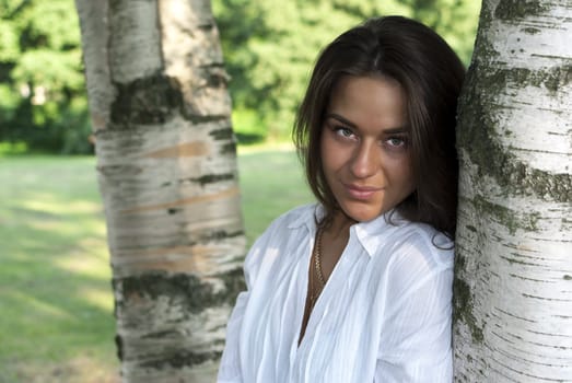 Cute girl in a white shirt standing near the birches