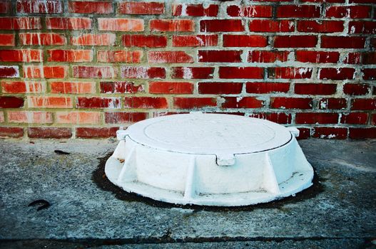 The white manhole against a brick wall in style grunge