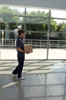 Side view of delivery woman in uniform pushing stack of cardboard boxes on dolly