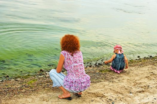 Mother and small daughter on the banks of reservoir in the period of rapid vegetation of green algae