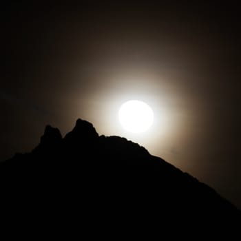 Moon shining bright behind black mountains