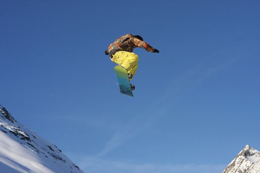 Young snowboarder jumping high over the mountains