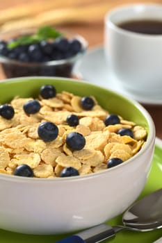 Sweet corn flakes with fresh blueberries with blueberries and a cup of coffee in the back (Selective Focus, Focus on the blueberries in the middle) 