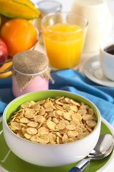 Sweetened corn flakes with yogurt, coffee, orange juice, fresh fruits and milk in the back (Selective Focus, Focus one third into the bowl)