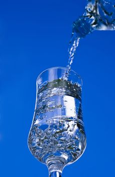 Pouring glass of water on the blue sky background